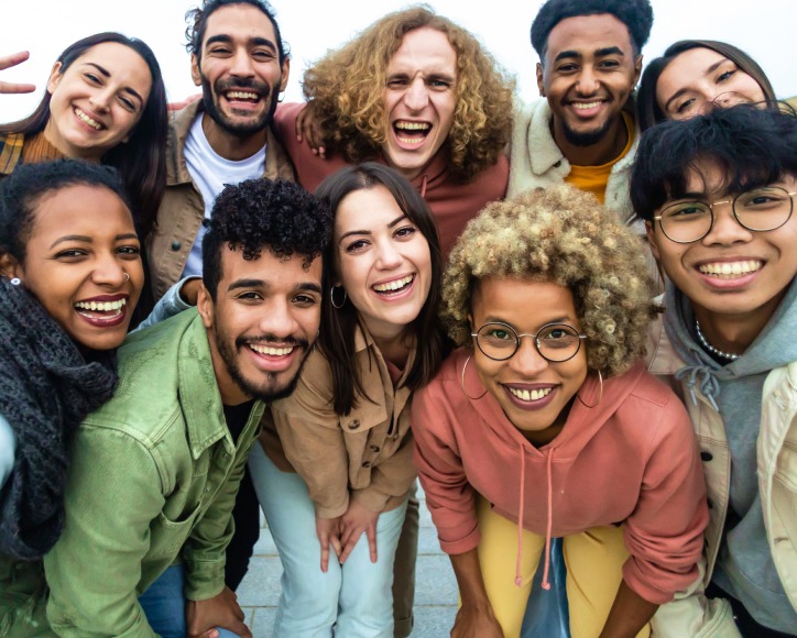 A group of ten young adults stand close together outdoors, smiling and looking at the camera.